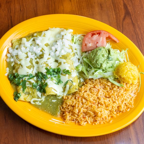 Green enchiladas with rice, guacamole, lettuce, tomato, and corn on a yellow plate.