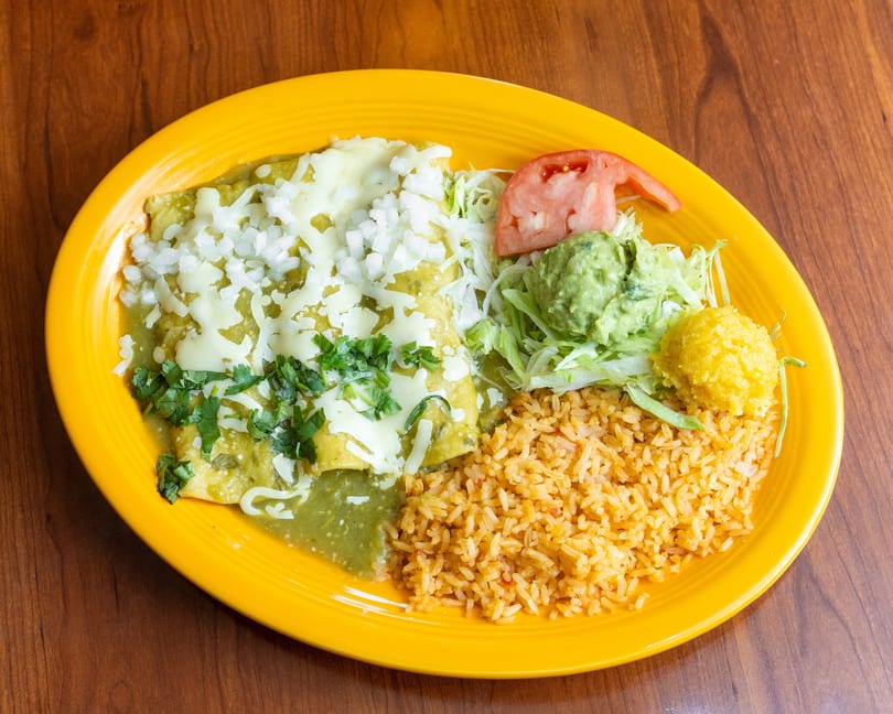 Green enchiladas with rice, guacamole, lettuce, tomato, and corn on a yellow plate.