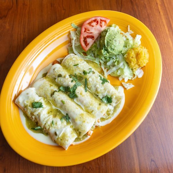 Three green enchiladas with sour cream, lettuce, guacamole, tomato, and corn on a yellow plate.