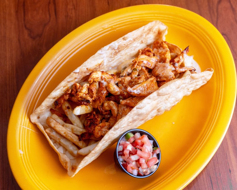 A crispy fried tortilla filled with seasoned chicken, french fries, and a side of pico de gallo.