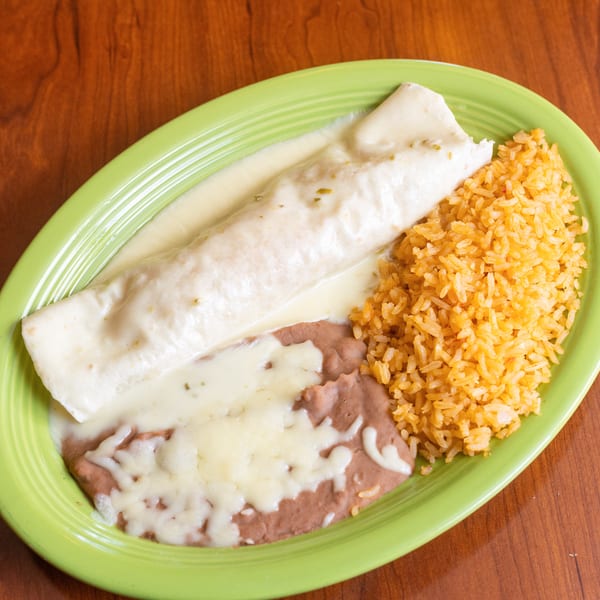 A burrito covered in white sauce, with a side of rice and refried beans, on a green plate.