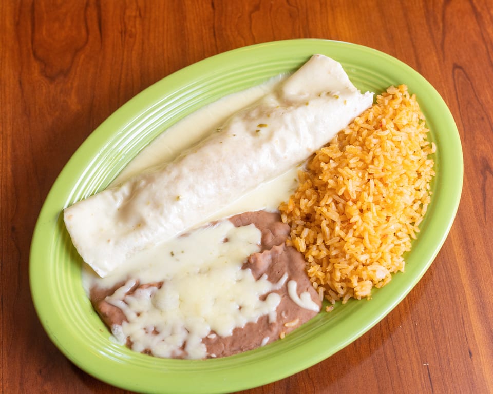 A burrito covered in white sauce, with a side of rice and refried beans, on a green plate.