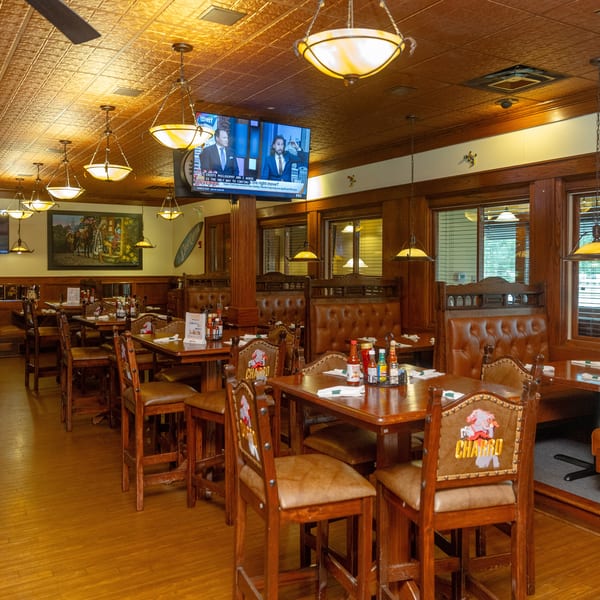A restaurant dining room with wooden tables, leather chairs, booths, and multiple TVs on the walls.