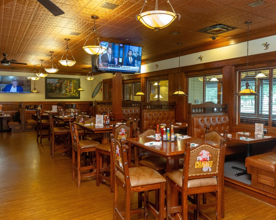 A restaurant dining room with wooden tables, leather chairs, booths, and multiple TVs on the walls.