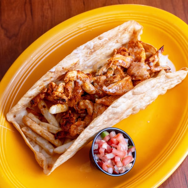 A large burrito with chicken, fries, and sauce, served with a side of pico de gallo.