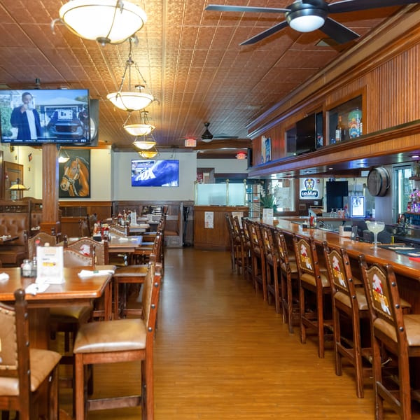 Spacious restaurant interior with wooden tables, brown booths, a long bar with stools, and TVs on the walls.