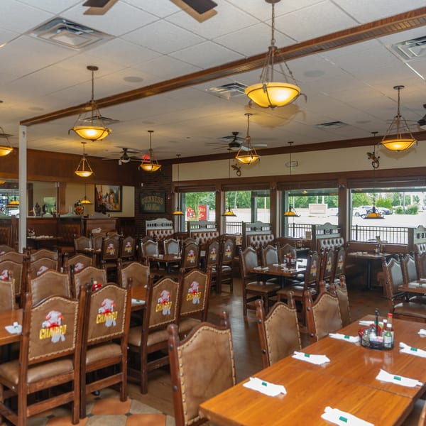 Spacious restaurant dining room with many empty tables and chairs, featuring large windows and warm lighting.