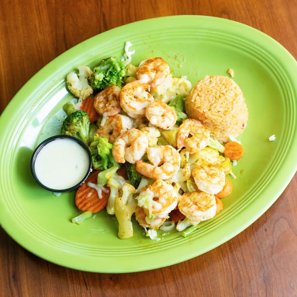 Shrimp with mixed vegetables, rice, and a side of white sauce on a green plate.