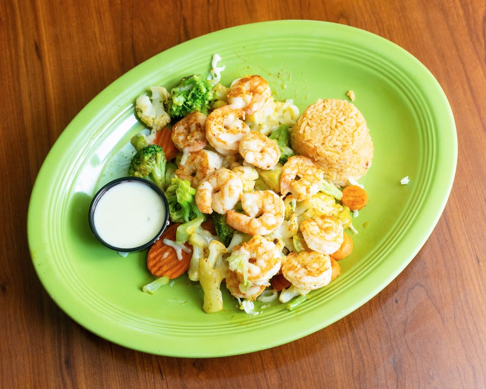 Shrimp with mixed vegetables, rice, and a side of white sauce on a green plate.