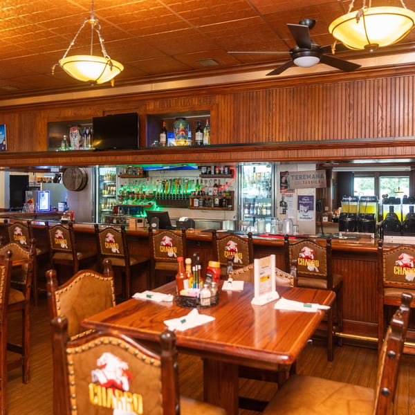 A restaurant bar area with wooden paneling, bar stools, and a fully stocked bar with liquor bottles.