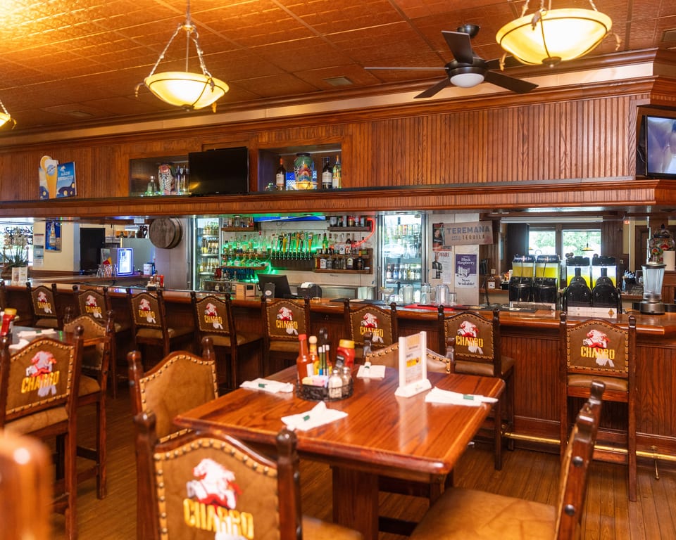 A restaurant bar area with wooden paneling, bar stools, and a fully stocked bar with liquor bottles.