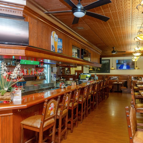 A long, empty bar with stools and a dining area with tables and booths.