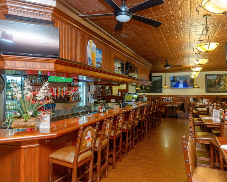 A long, empty bar with stools and a dining area with tables and booths.