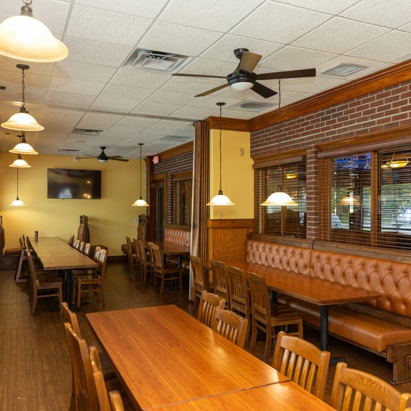 Warmly lit restaurant interior with wooden tables, chairs, and brown leather booth seating along brick walls.