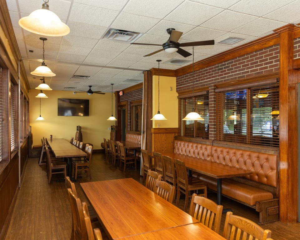 Warmly lit restaurant interior with wooden tables, chairs, and brown leather booth seating along brick walls.