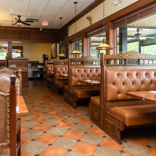 Restaurant interior with rows of empty brown leather booths, wooden tables, and checkered floor tiles.