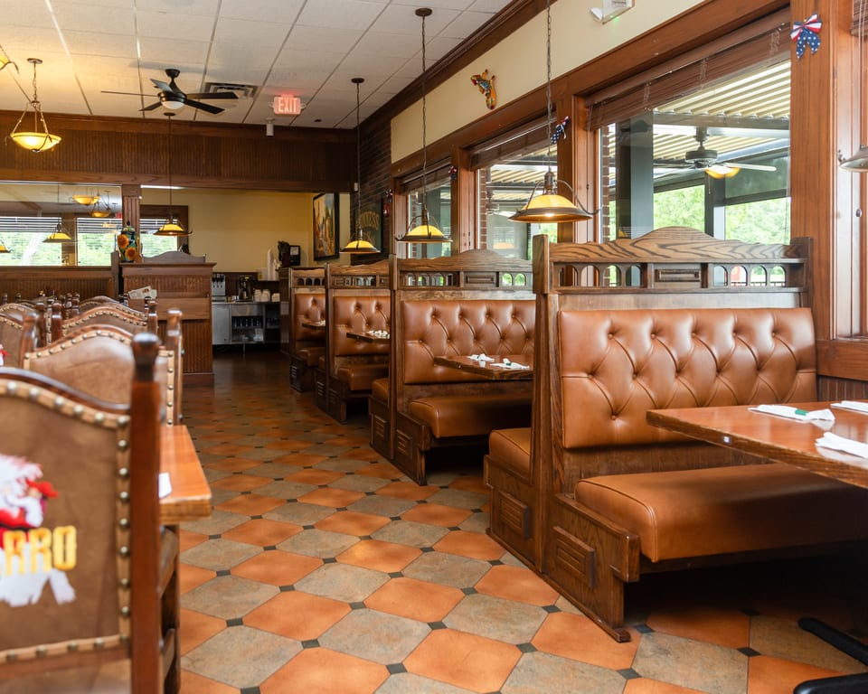Restaurant interior with rows of empty brown leather booths, wooden tables, and checkered floor tiles.