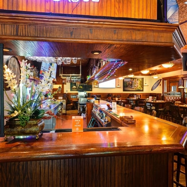 Warmly lit restaurant interior with a wooden bar, dining tables, booths, and a specials sign.